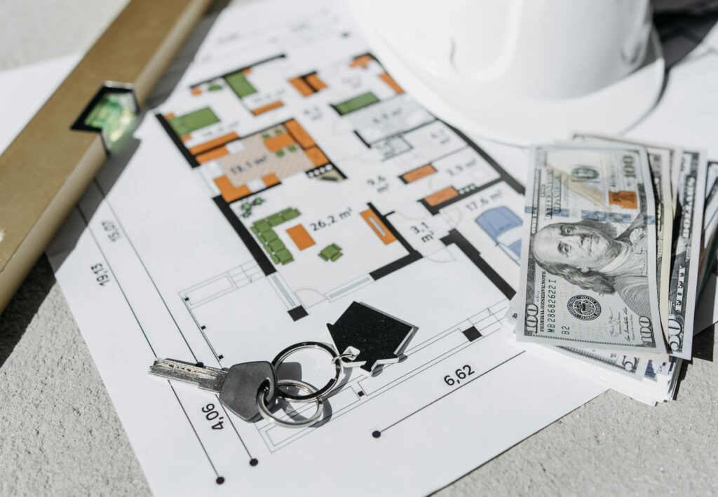Floor plan with cash, keys, and hard hat symbolizing real estate investment and property planning.