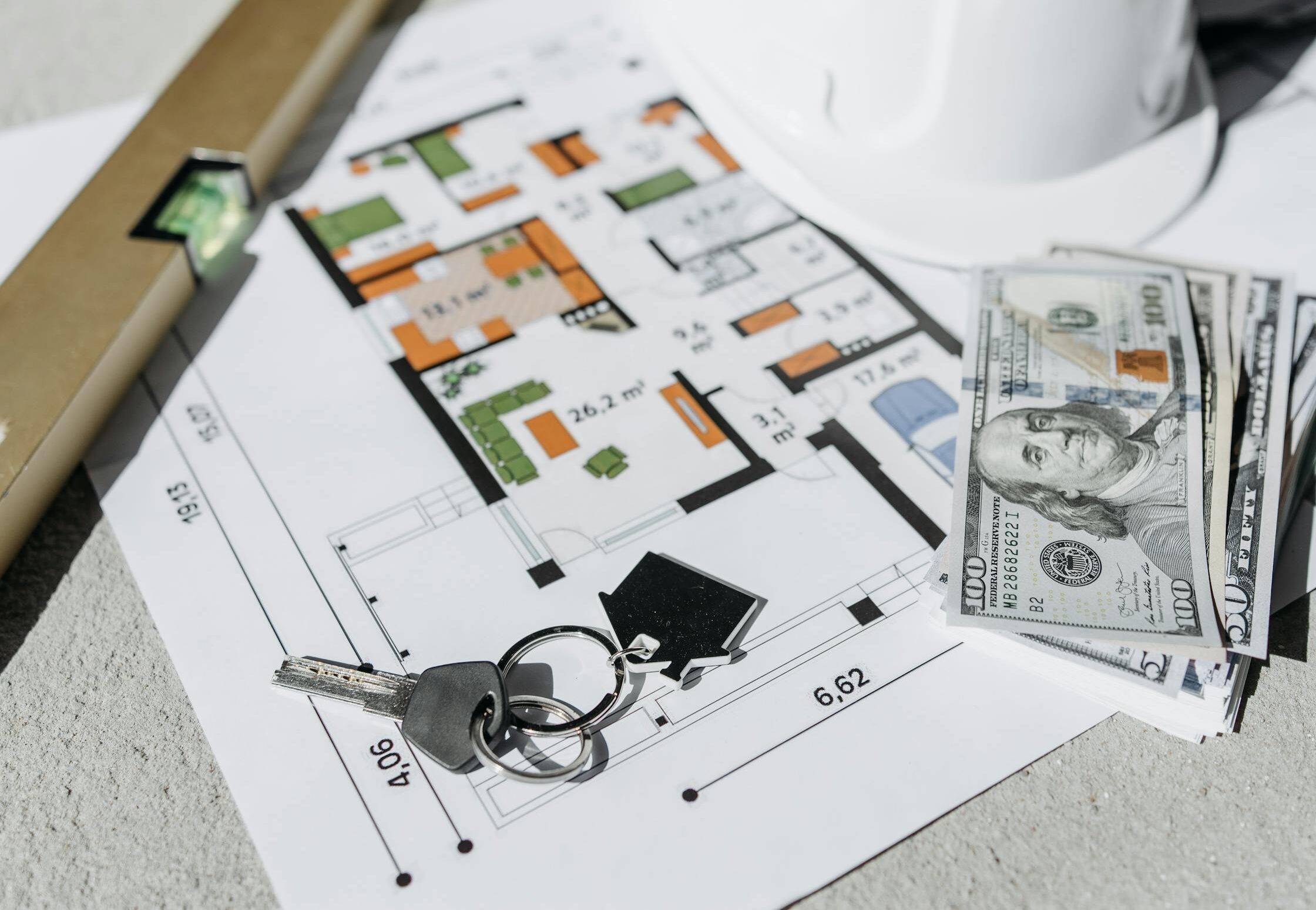 Floor plan with cash, keys, and hard hat symbolizing real estate investment and property planning.