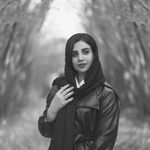 Black and white photo of a woman in a black leather jacket and headscarf posing in a forest in Hamedan.
