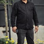 Casually dressed man with glasses standing outdoors, conveying confidence.