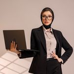 Confident woman in a suit holding a laptop, symbolizing professionalism and tech-savvy.