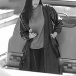 Portrait of a young woman in black and white beside a vintage car, exuding style and elegance.