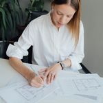 Woman architect reviewing floor plans at a desk indoors, surrounded by plants.